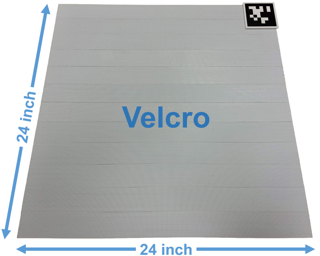 A 24 by 24 inch board covered edge to edge in strips of hook-side Velcro, with a fiducial marker in its top-right corner.